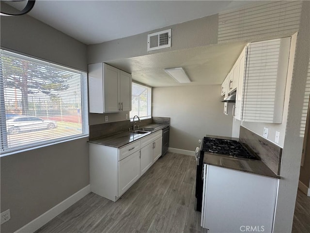 kitchen with white cabinets, dark countertops, visible vents, and a sink