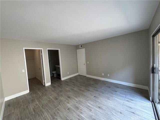 unfurnished bedroom featuring connected bathroom, baseboards, wood finished floors, a spacious closet, and visible vents