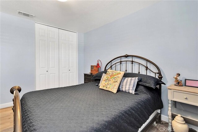 bedroom featuring baseboards, visible vents, wood finished floors, and a closet