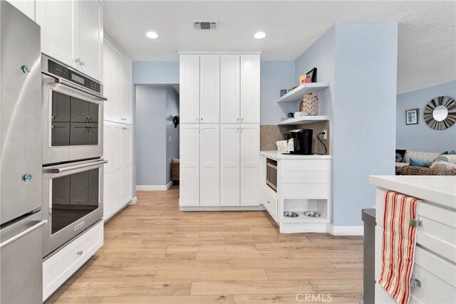 kitchen featuring white cabinets, open shelves, appliances with stainless steel finishes, light wood-type flooring, and visible vents