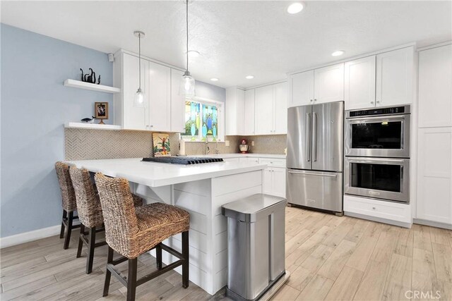 kitchen with open shelves, a kitchen breakfast bar, light wood-style flooring, stainless steel appliances, and white cabinetry