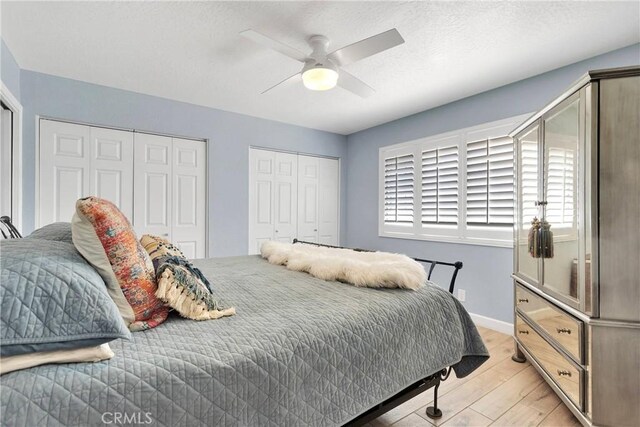 bedroom with baseboards, a ceiling fan, two closets, and light wood finished floors