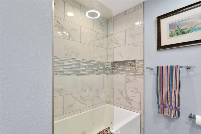bathroom with a textured wall and a combined bath / shower with jetted tub