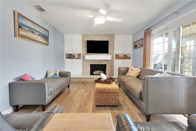living area with a fireplace, a ceiling fan, visible vents, and light wood-style floors