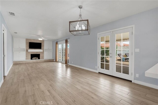 unfurnished living room featuring french doors, baseboards, ceiling fan with notable chandelier, and light wood-type flooring