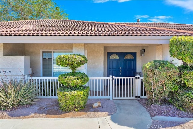 view of exterior entry featuring a tiled roof, a gate, and stucco siding