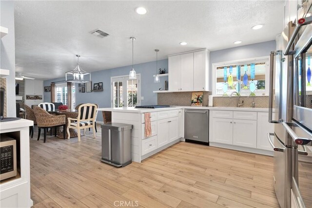 kitchen featuring appliances with stainless steel finishes, a peninsula, white cabinetry, decorative backsplash, and visible vents