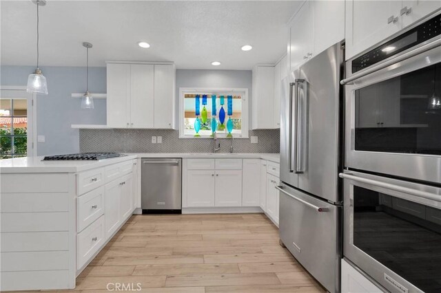 kitchen featuring light wood-style floors, a peninsula, tasteful backsplash, and stainless steel appliances