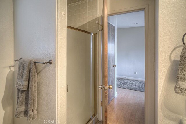 bathroom featuring a textured wall, wood finished floors, and a shower stall