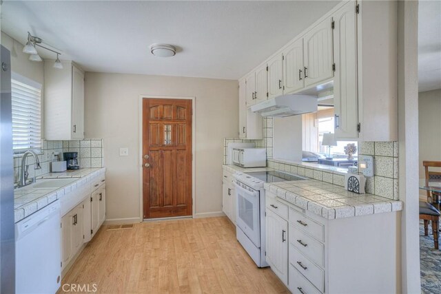 kitchen with white cabinets, light wood-style floors, white appliances, backsplash, and under cabinet range hood