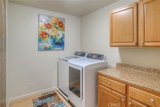 laundry area featuring cabinet space, washing machine and clothes dryer, light wood finished floors, baseboards, and visible vents