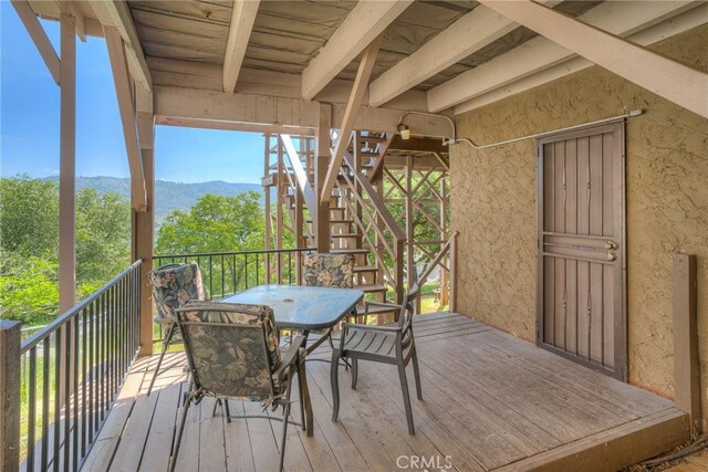 wooden deck with a mountain view, outdoor dining area, and stairway