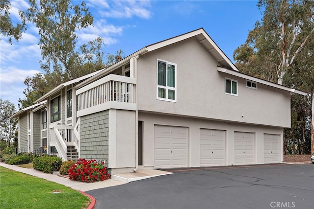 view of side of property featuring a garage, a balcony, stucco siding, and driveway