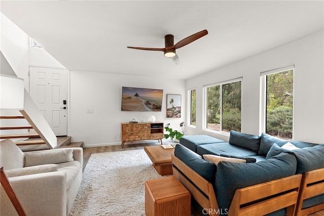 living room featuring stairs, a ceiling fan, baseboards, and wood finished floors