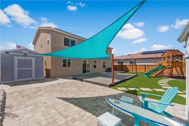rear view of property featuring a shed, a fenced backyard, an outbuilding, a playground, and a patio