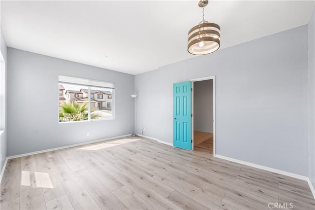 empty room featuring an inviting chandelier, baseboards, and wood finished floors