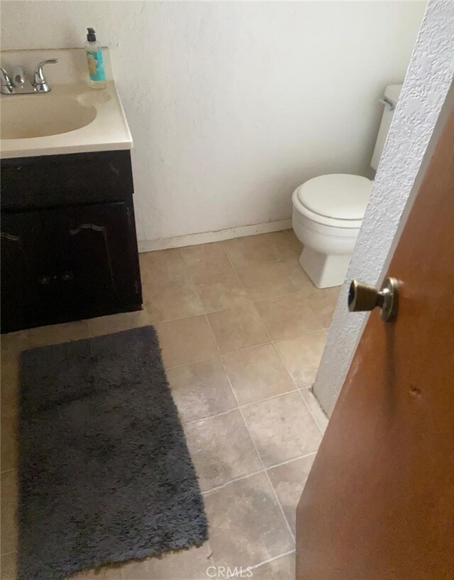 half bath featuring vanity, baseboards, tile patterned floors, and toilet
