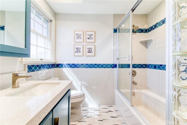 bathroom featuring tile walls, a wainscoted wall, bath / shower combo with glass door, vanity, and toilet