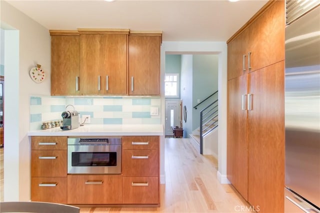 kitchen with backsplash, stainless steel appliances, brown cabinetry, and light wood-type flooring