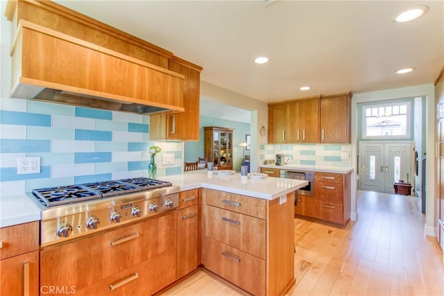 kitchen featuring light countertops, a peninsula, stainless steel gas stovetop, custom range hood, and tasteful backsplash