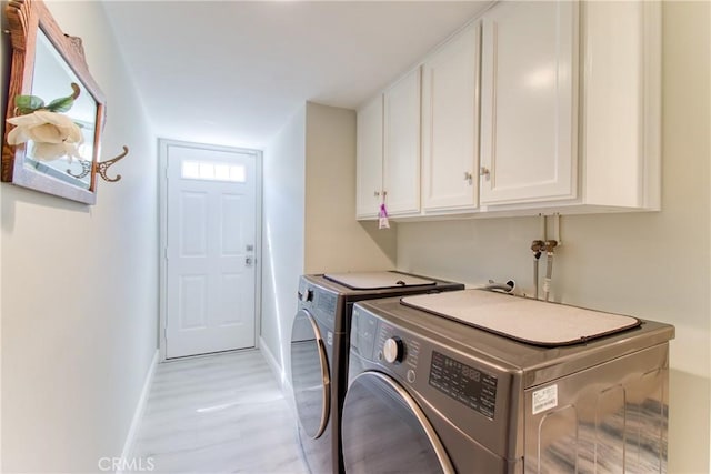 clothes washing area with baseboards, light wood-type flooring, cabinet space, and washer and dryer