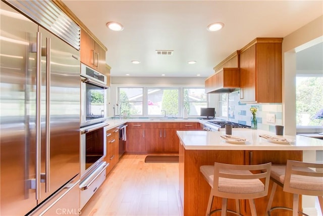 kitchen with visible vents, brown cabinetry, a peninsula, appliances with stainless steel finishes, and a warming drawer