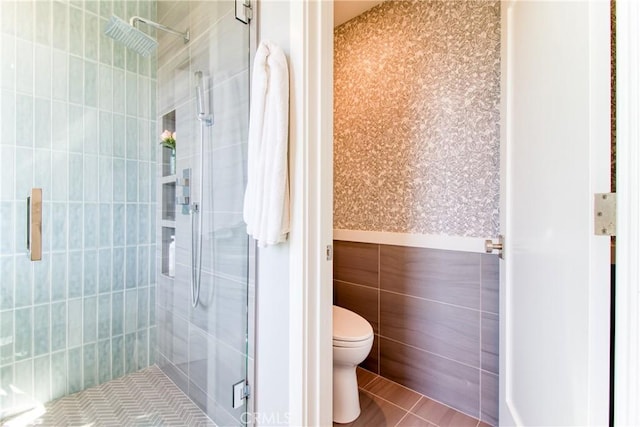 full bath with toilet, tile walls, wallpapered walls, tile patterned floors, and a shower stall