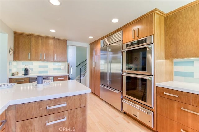 kitchen featuring backsplash, appliances with stainless steel finishes, light countertops, light wood-style floors, and a warming drawer