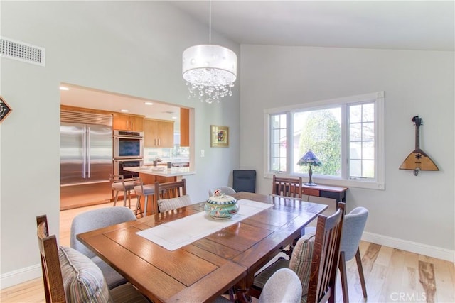 dining area with visible vents, baseboards, high vaulted ceiling, light wood-style flooring, and a notable chandelier