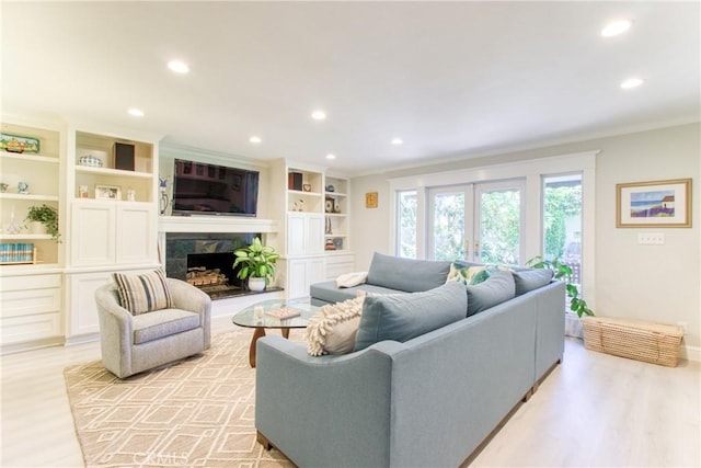 living area with crown molding, recessed lighting, a fireplace with raised hearth, and light wood-type flooring