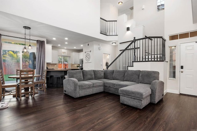 living area featuring baseboards, a high ceiling, dark wood-style flooring, and stairs