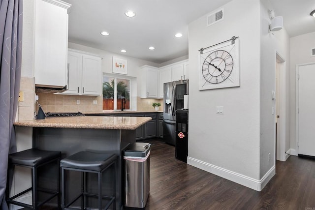 kitchen featuring a peninsula, white cabinetry, stainless steel fridge with ice dispenser, and tasteful backsplash