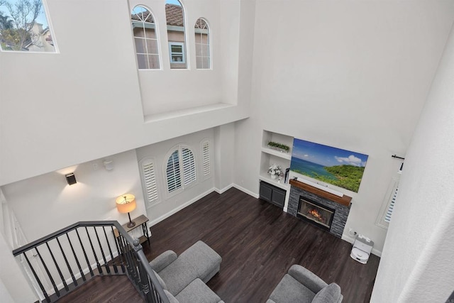 living area featuring built in features, a glass covered fireplace, wood finished floors, baseboards, and a high ceiling