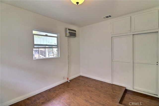 unfurnished bedroom with dark wood-style flooring, baseboards, visible vents, a wall mounted AC, and a closet