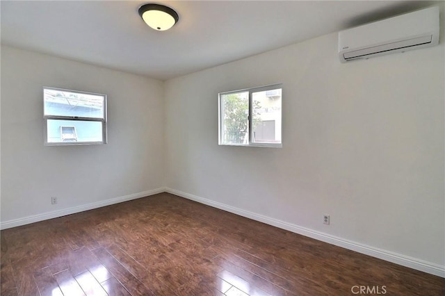 empty room featuring a wall mounted AC, a healthy amount of sunlight, and dark wood-style floors