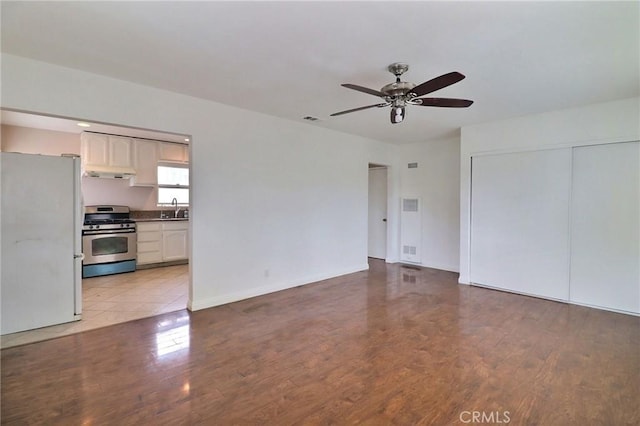 unfurnished living room featuring a ceiling fan, visible vents, a sink, and wood finished floors