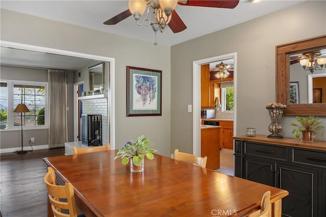 dining space featuring a brick fireplace, a ceiling fan, baseboards, and wood finished floors
