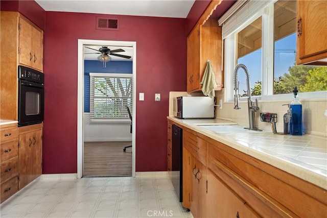 kitchen with a ceiling fan, light floors, tile counters, a sink, and black appliances