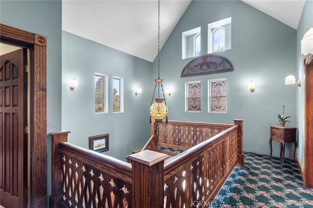 hallway with carpet flooring, high vaulted ceiling, and an upstairs landing