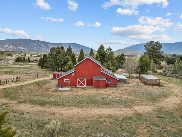 view of barn featuring fence, a mountain view, and a rural view