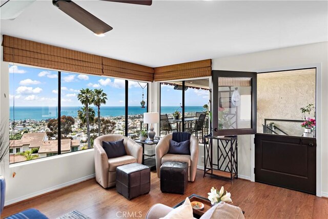 sunroom / solarium featuring baseboards, a water view, and wood finished floors