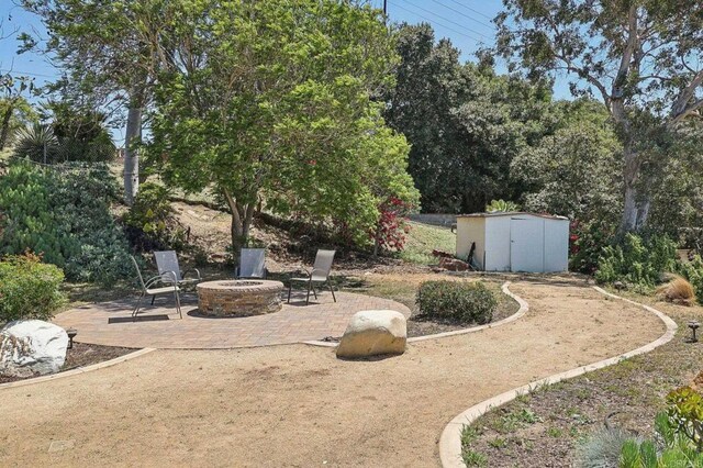 view of yard with an outdoor structure, a fire pit, a patio area, and a storage shed
