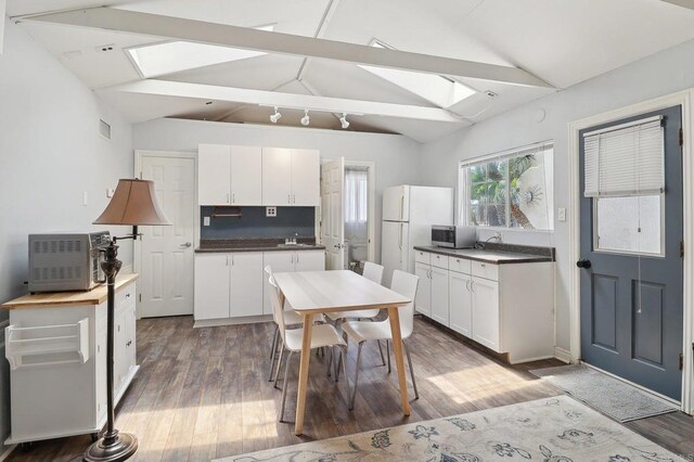 kitchen featuring lofted ceiling with skylight, dark countertops, stainless steel microwave, and freestanding refrigerator