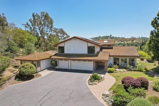 split level home with driveway, a tile roof, roof mounted solar panels, an attached garage, and stucco siding