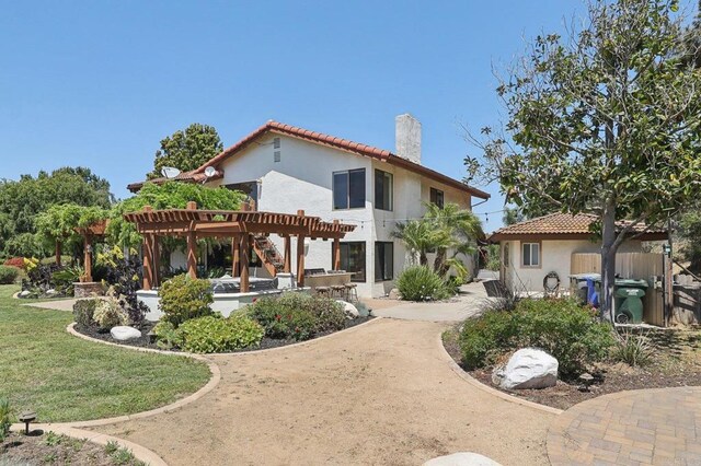 back of house featuring a pergola, stucco siding, a chimney, a patio area, and a yard
