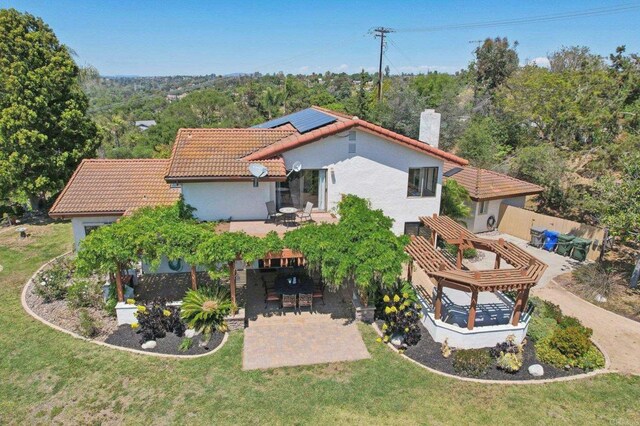 rear view of property with a tiled roof, a chimney, solar panels, a patio, and stucco siding