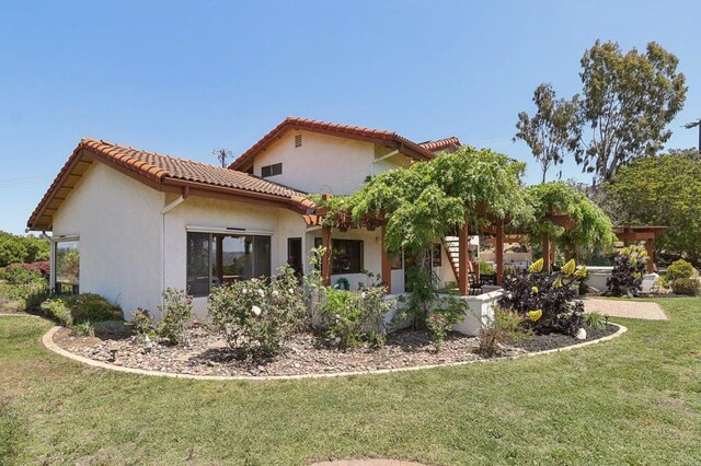 back of house featuring a lawn, stucco siding, and a tiled roof