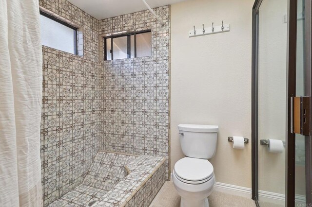 bathroom featuring toilet, baseboards, and tiled shower