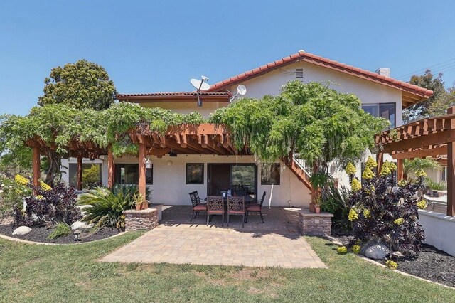 rear view of property with a pergola, a tile roof, stucco siding, a patio area, and a yard