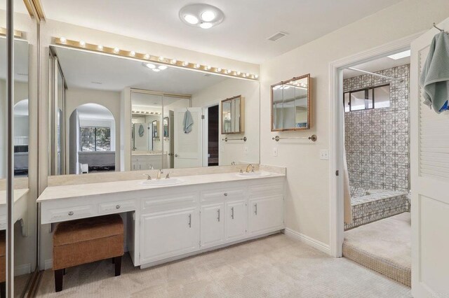 bathroom with double vanity, visible vents, a tile shower, and a sink